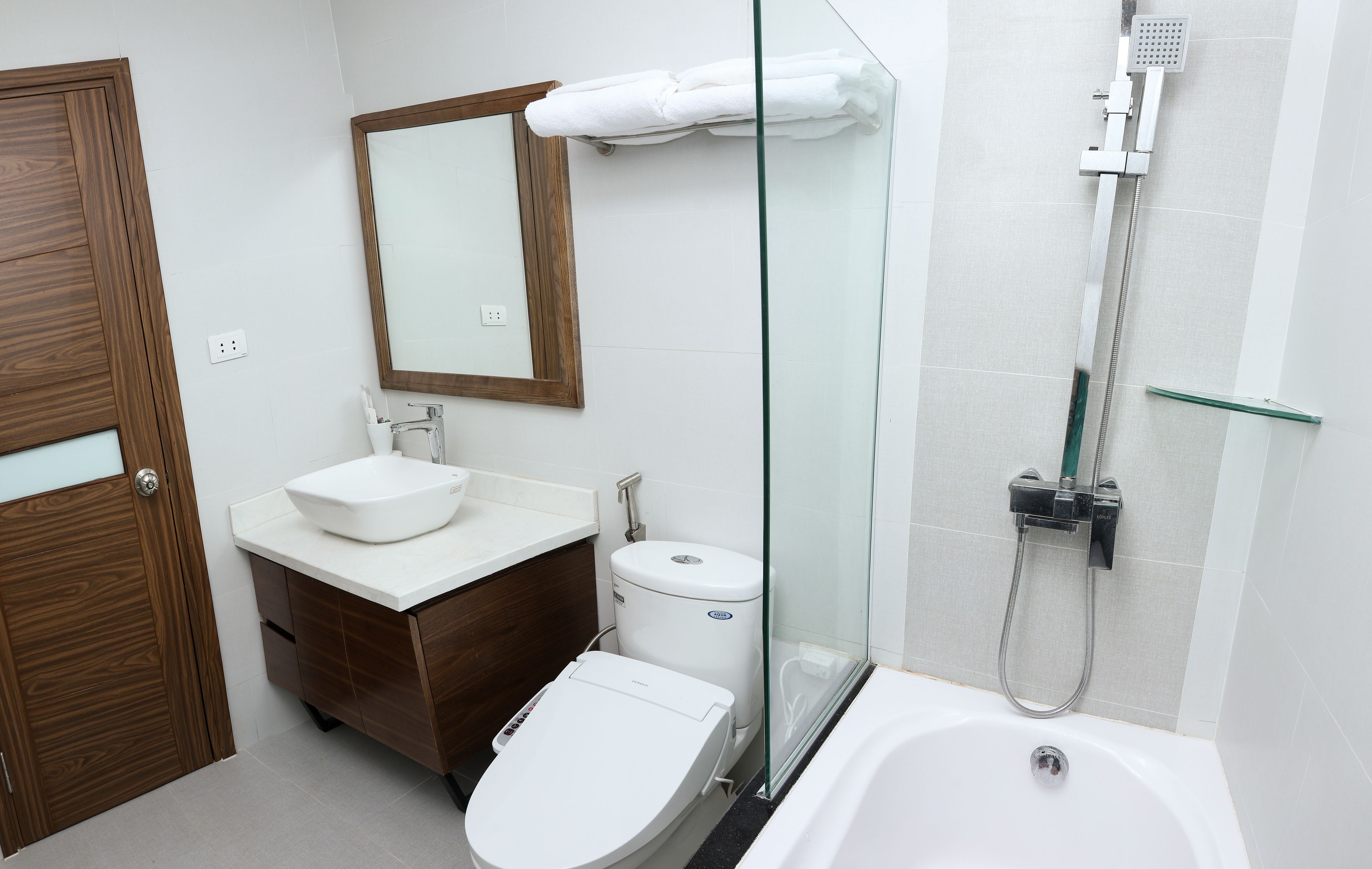 A modern bathroom with a wooden vanity, a white toilet, a glass shower enclosure, and a bathtub.