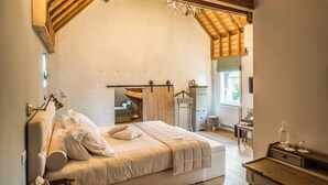 Un dormitorio con cama alta, vigas de madera, un escritorio y una ventana.