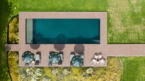 An aerial view of a rectangular swimming pool with a brick deck, surrounded by a grassy area with small water features. - Villa Copis (Borgloon)