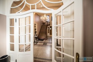 Eine offene Tür führt zu einer Treppe mit einem Chandelier, Teppichstufen und Blick in einen Raum mit einer Tür und einem Mülleimer.