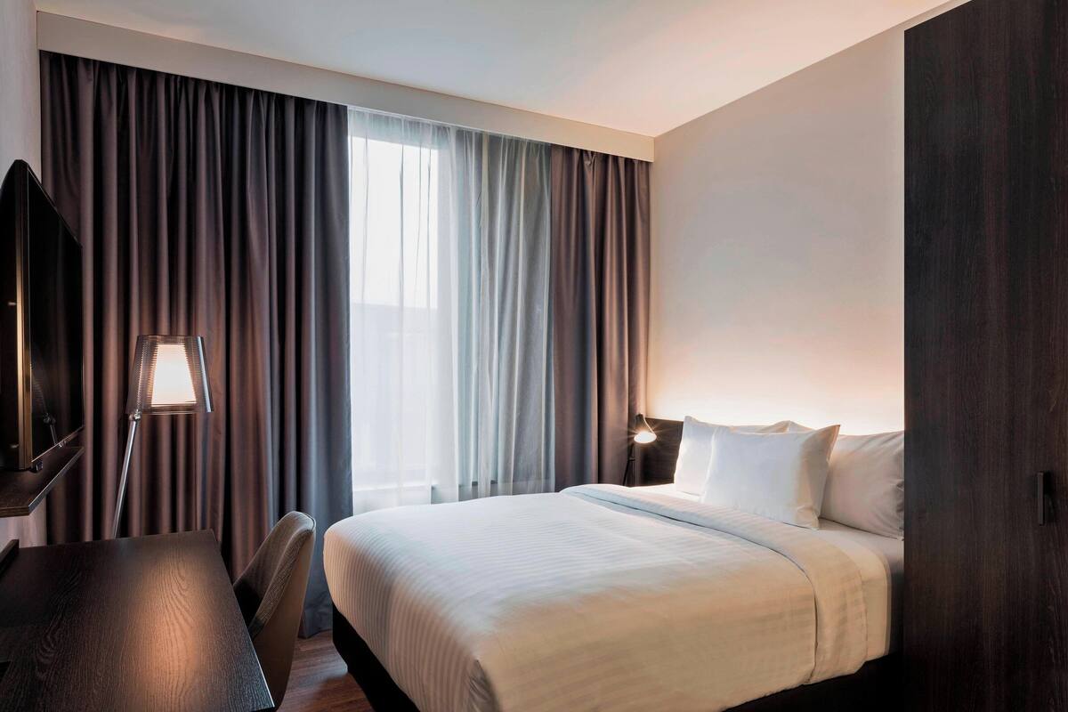 Ein Hotelzimmer mit Bett, Schreibtisch, Lampe und Fernseher.