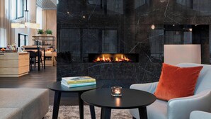 A modern living room with a black marble fireplace, a white sofa with an orange pillow, and a small round table with a book and candle. - Residence Inn by Marriott Frankfurt City Center (Frankfurt)