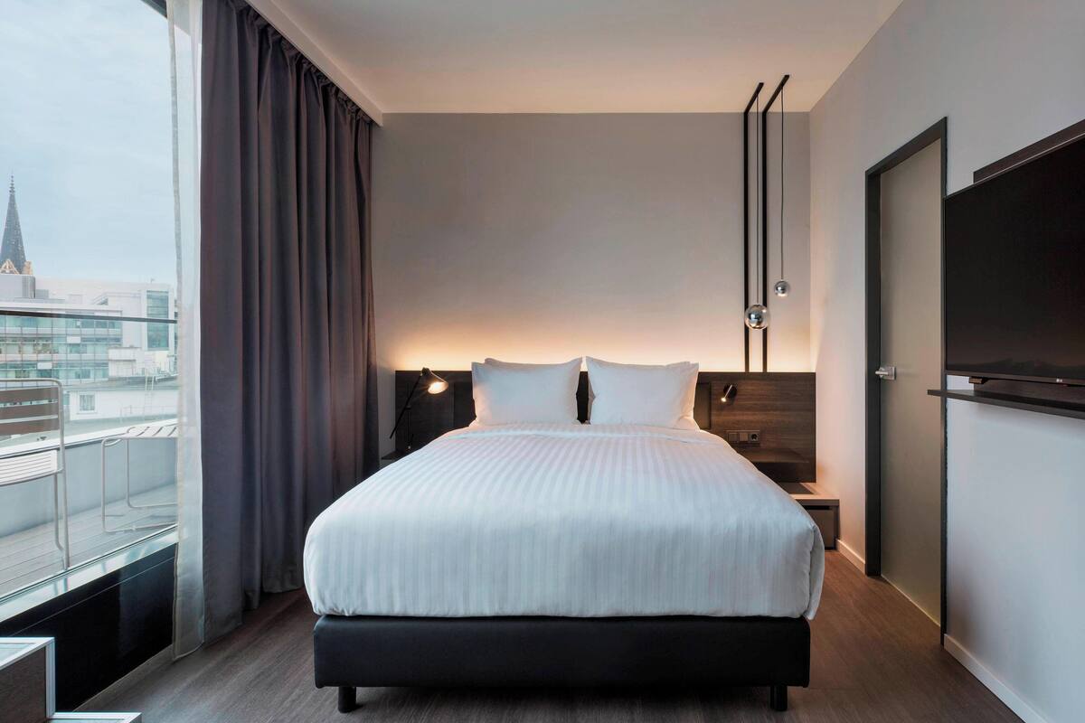Ein modernes Hotelzimmer mit einem großen Bett, einem an der Wand befestigten Fernseher und Blick auf die Stadt.