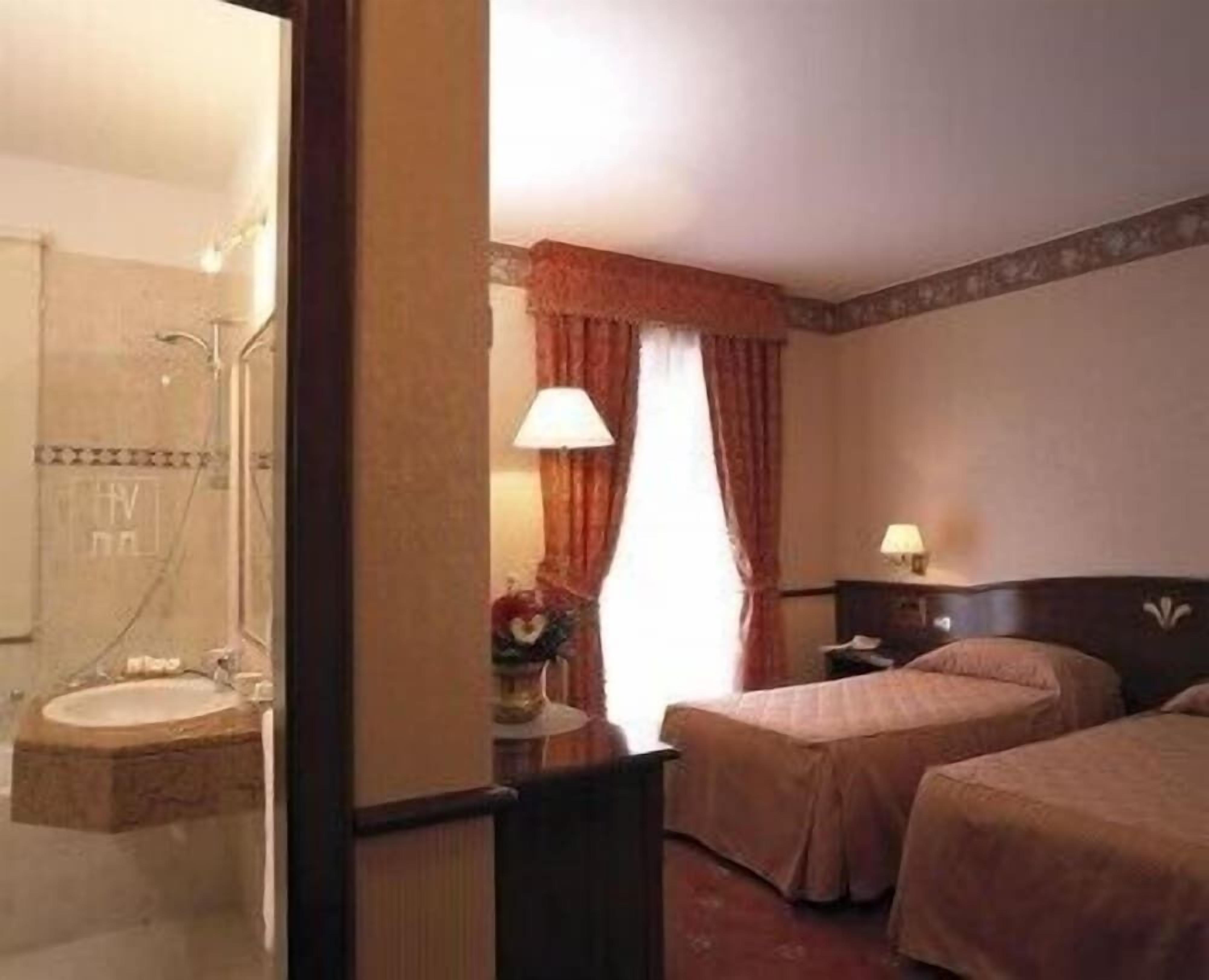 Una camera d'albergo con bagno, un letto, un comodino e una lampada.