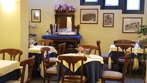 Un comedor con sillas y mesas de madera, un mueble de madera con un arreglo floral y cuadros en la pared.