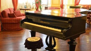 Un piano de cola en una habitación amplia con un sofá rojo y una mesa de comedor.
