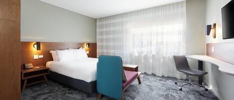 A hotel room with a bed, a desk, a chair, a telephone, and a TV.
