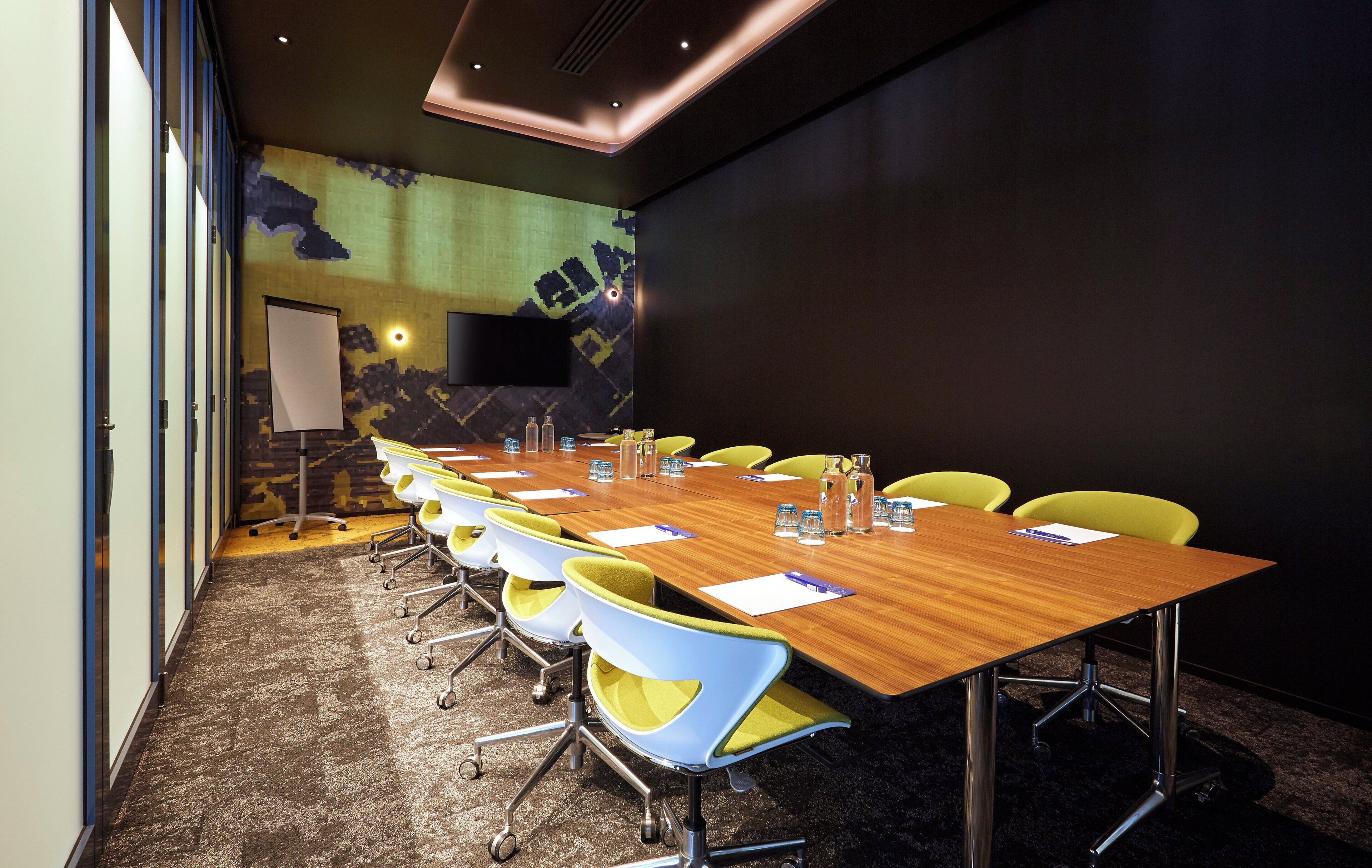 A conference room with a long table, yellow chairs, and a projector screen.