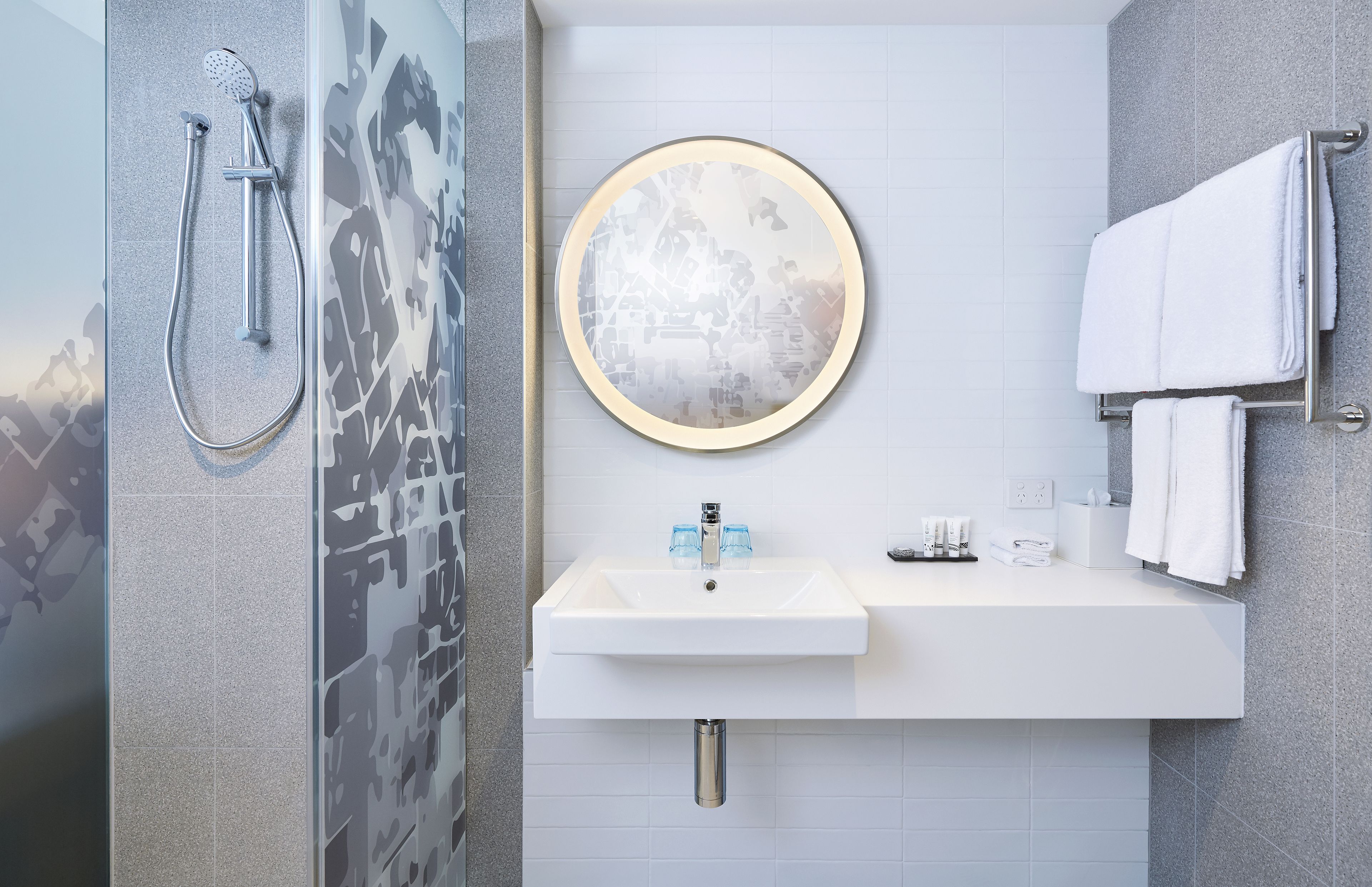 Een moderne badkamer met een douche, wastafel en handdoekrek.