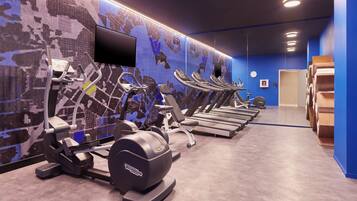 A gym with multiple treadmills, stationary bikes, and ellipticals, with a large digital screen on the wall.