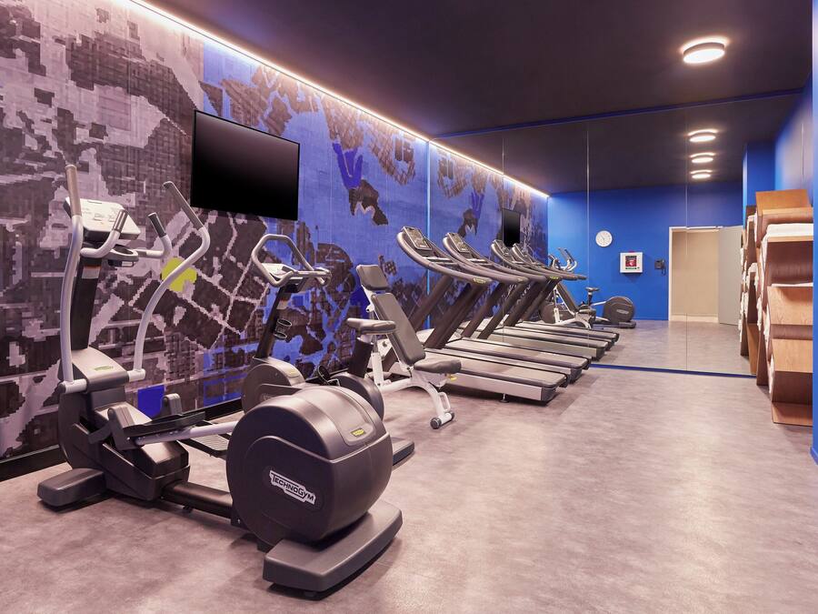 A gym with multiple treadmills, stationary bikes, and ellipticals, with a large digital screen on the wall.