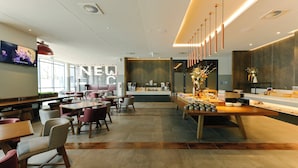 Un restaurante moderno con una barra larga, zona de estar y una pantalla de televisión que muestra una banda.