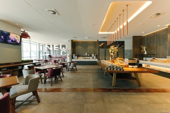 A modern restaurant with a long counter, seating area, and a television screen displaying a band. - Holiday Inn Express Newcastle by IHG (Newcastle West)