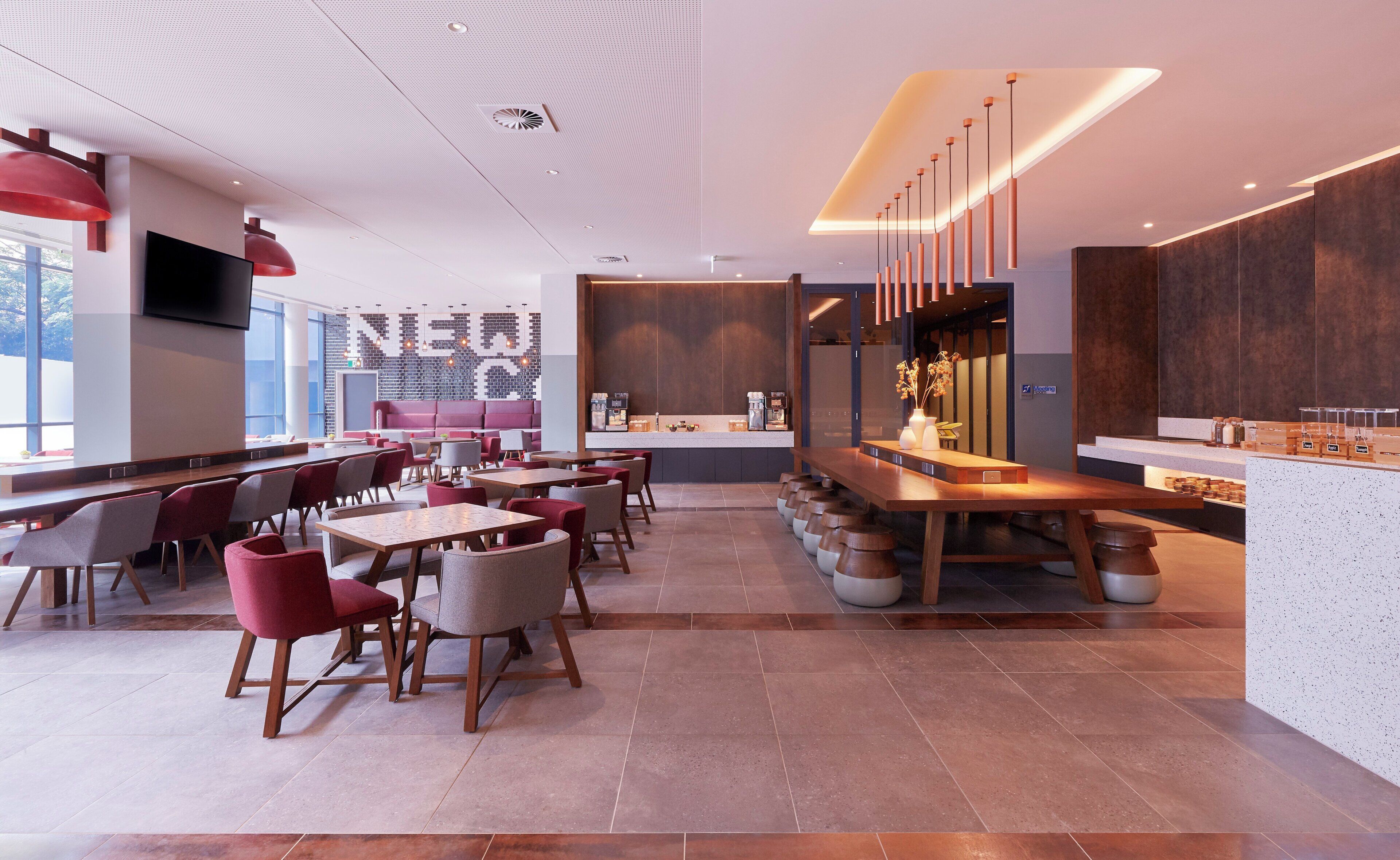 Een modern restaurantinterieur met een lange toonbank, diverse zitmogelijkheden en een groot televisiescherm.