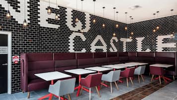 A restaurant interior with a black and white tiled wall, red cushioned booths, and grey and red chairs.