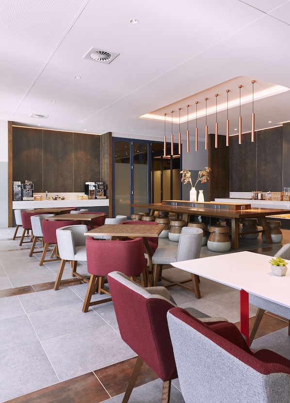 A modern dining area with wooden tables and chairs, a central bar, and pendant lighting.