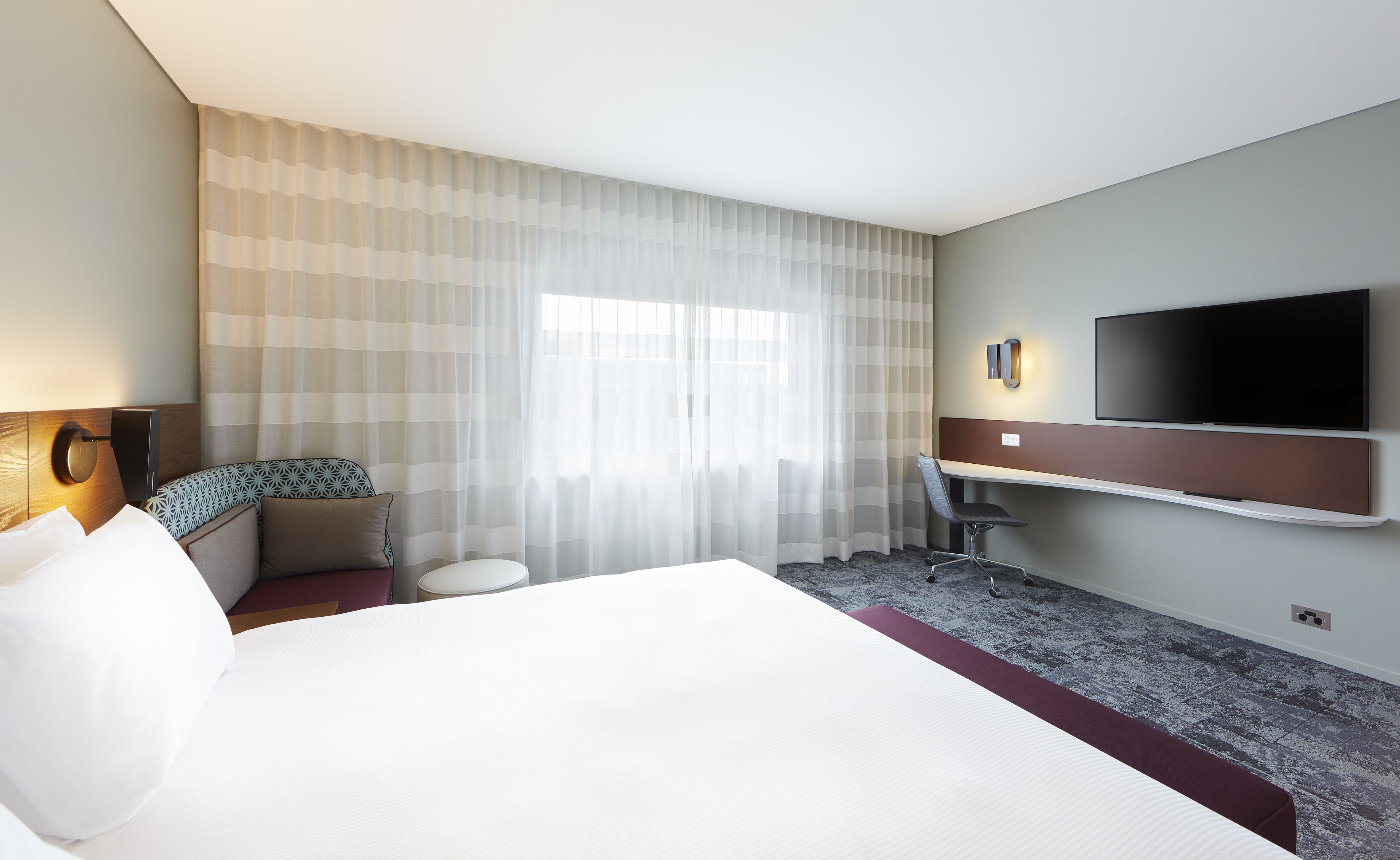 A hotel room with a bed, a desk, a chair, a television, and a window with curtains.