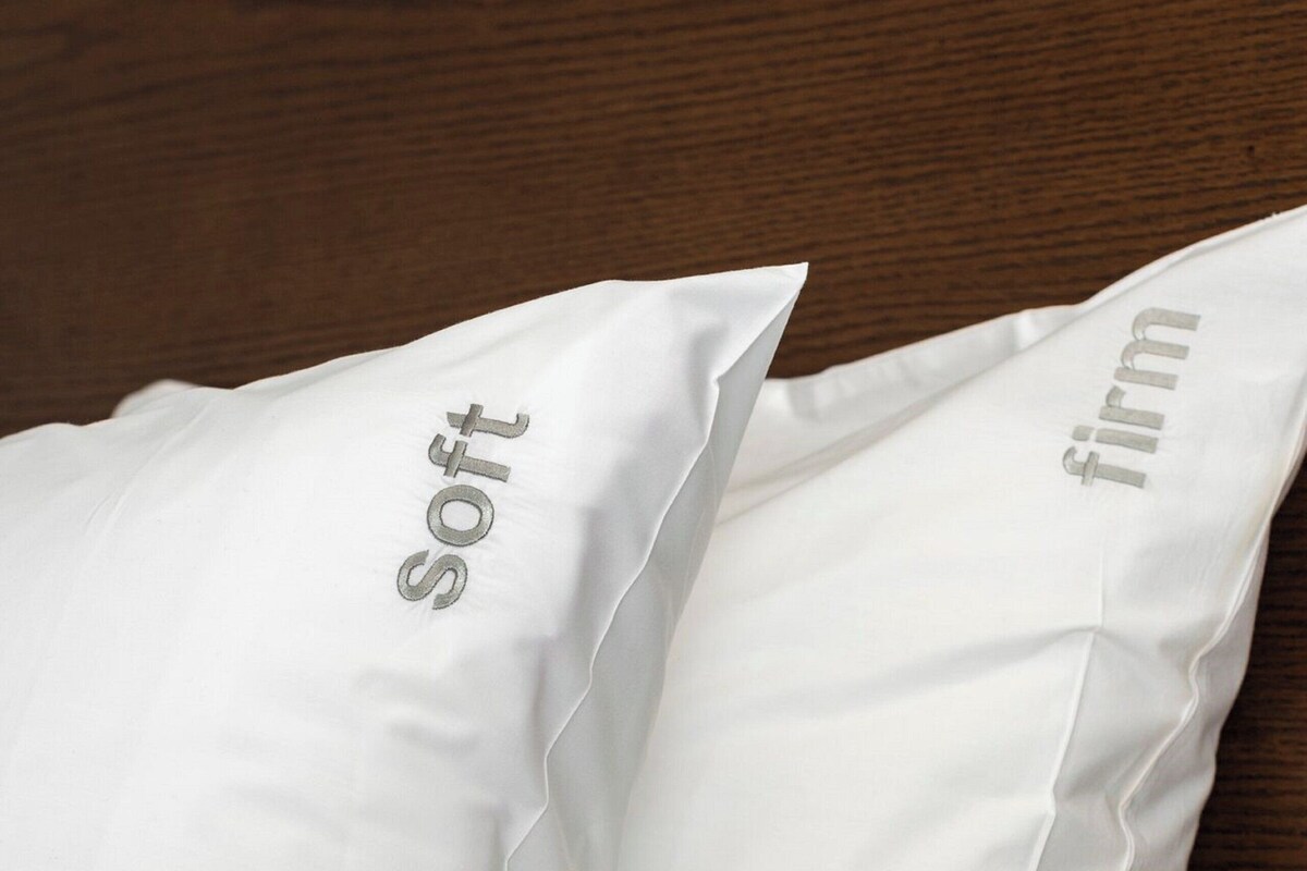 Two white pillows with the words "soft" and "firm" on them, placed on a bed with a wooden headboard.