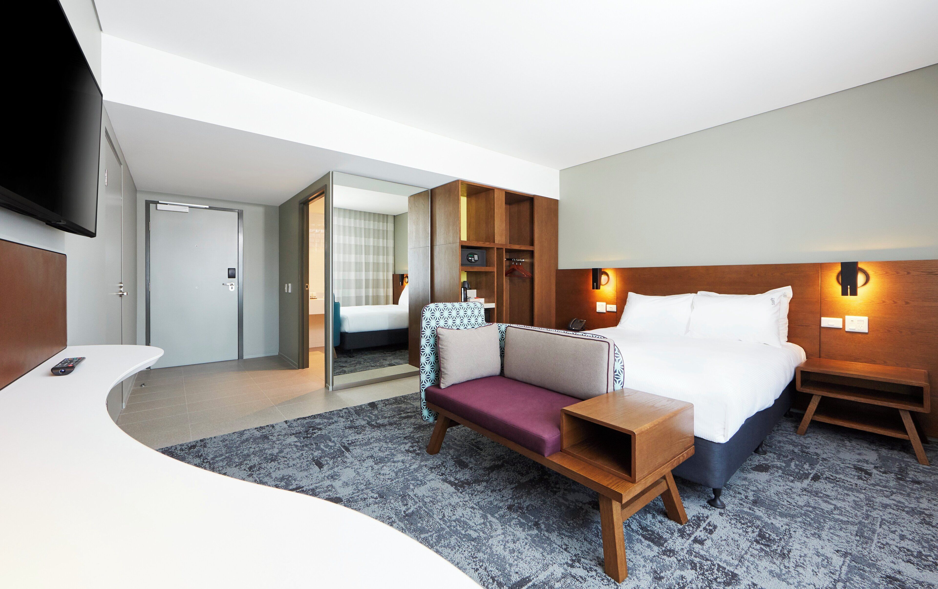 A hotel room with a bed, a sofa, a small table, a TV, and a wardrobe.