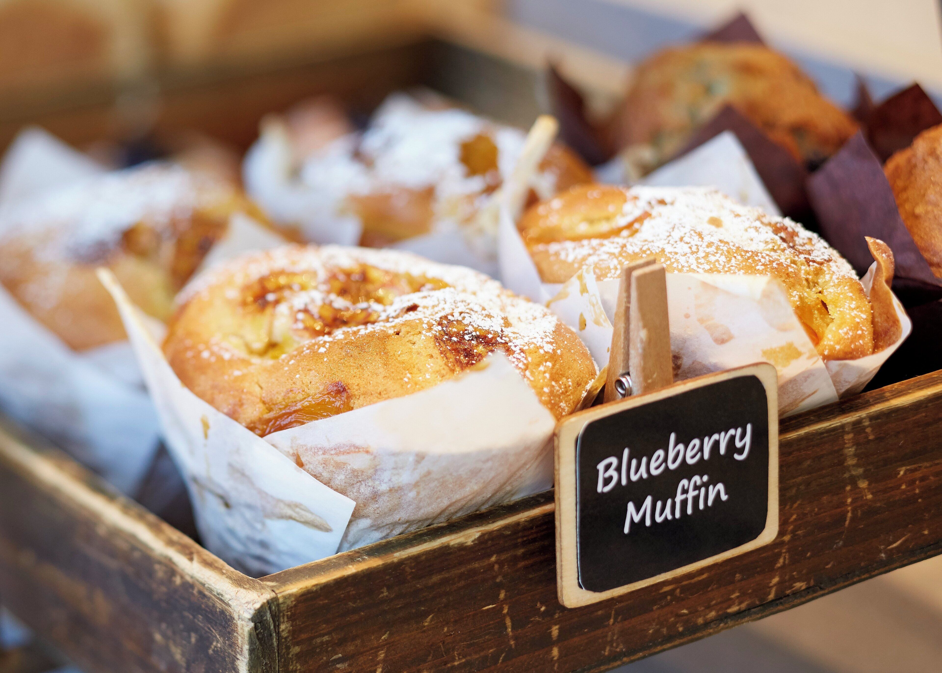 A tray of baked goods labeled 'Blueberry Muffin' with a wooden presentation board.
