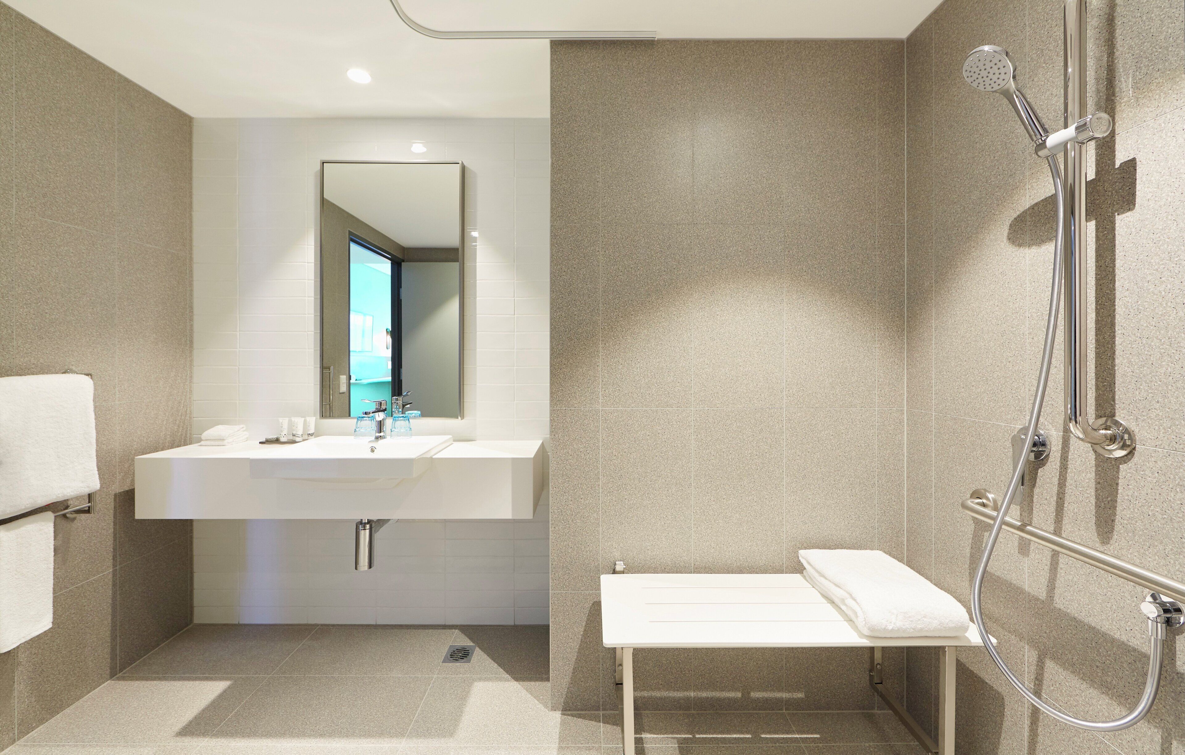 A modern bathroom with a sink, mirror, shower, and bench.