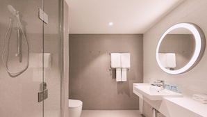Un baño moderno con ducha acristalada, inodoro, lavabo con espejo y toallero.