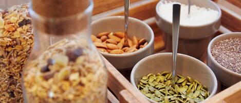 A wooden tray containing various food items including granola, nuts, and seeds.