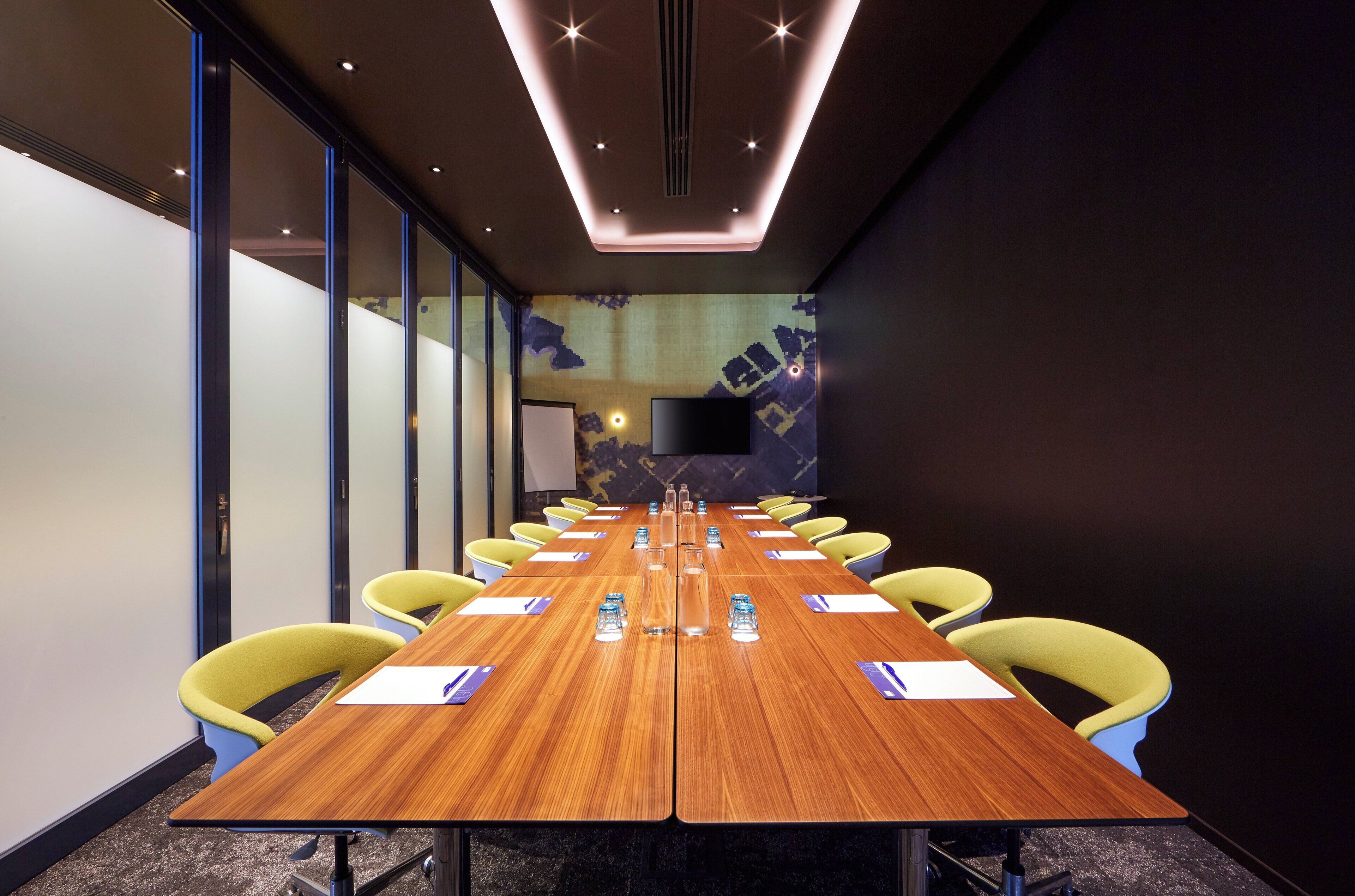 A conference room with a long wooden table, yellow chairs, and a flat-screen TV mounted on the wall.