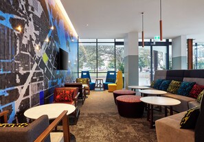 A modern interior with seating arrangements, a large window, and a wall-mounted television. - Holiday Inn Express Newcastle by IHG (Newcastle West)