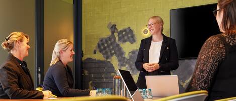 Ein Konferenzraum mit einem großen Bildschirm, einem Laptop und einer Wasserflasche auf dem Tisch.