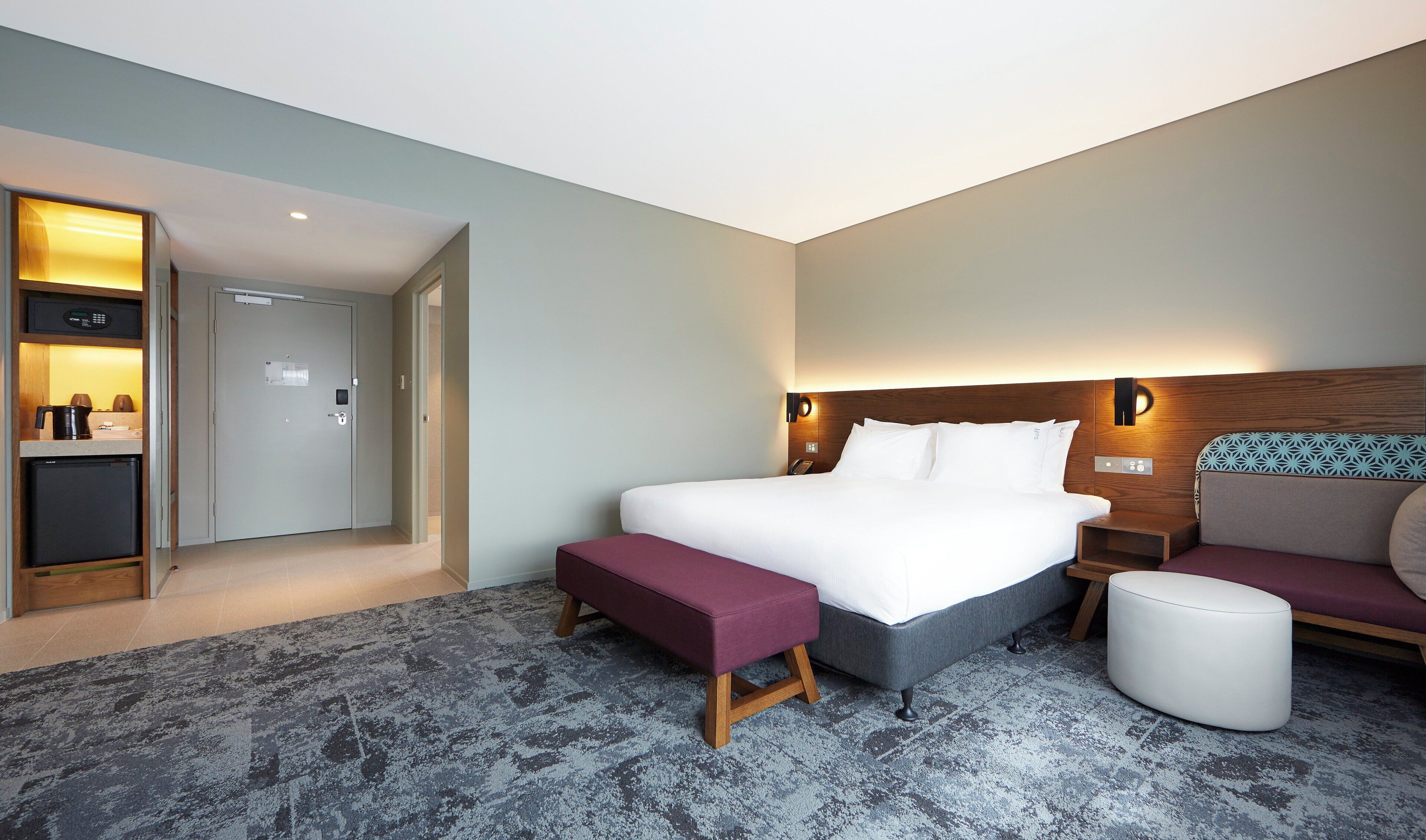 Een hotelkamer met een bed, een zithoek met een bankje, een kleine tafel, een aan de muur bevestigd telefoon en een deur naar een kitchenette.