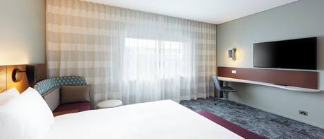A hotel room with a bed, a desk, a chair, a TV, and a window with curtains.