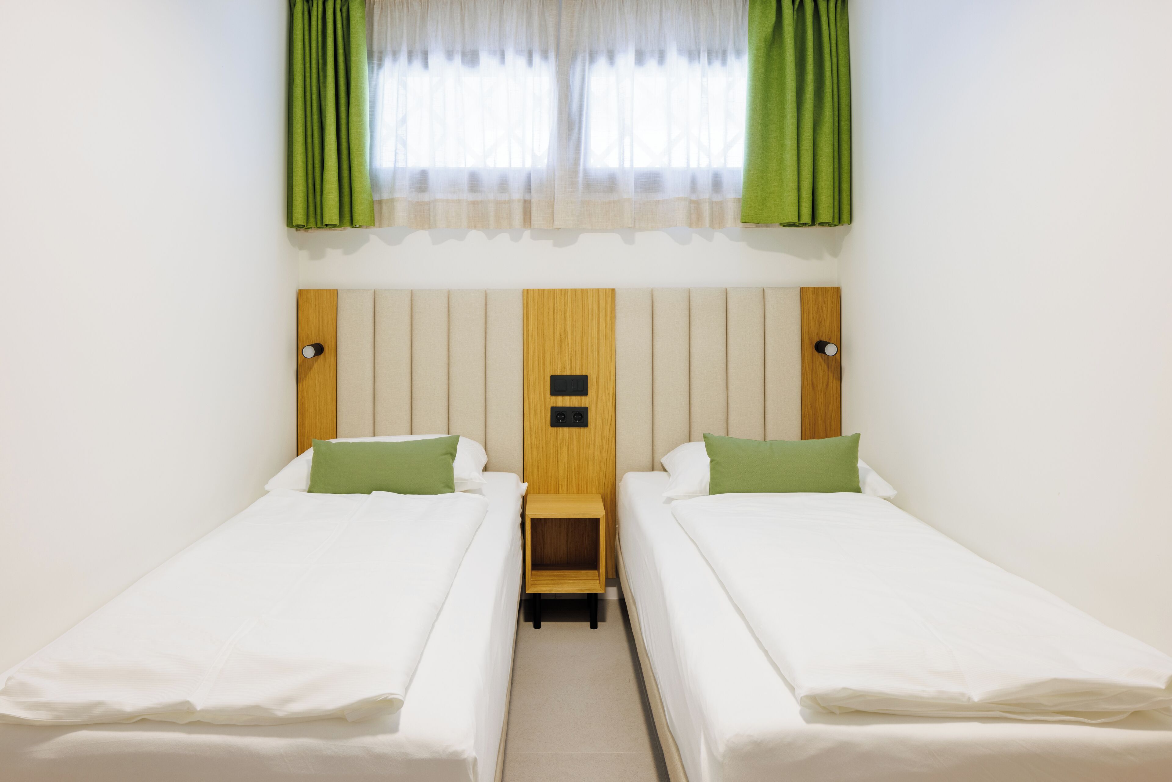 Una habitación con dos camas individuales, un cabecero de madera y una mesita de noche de madera entre ellas.
