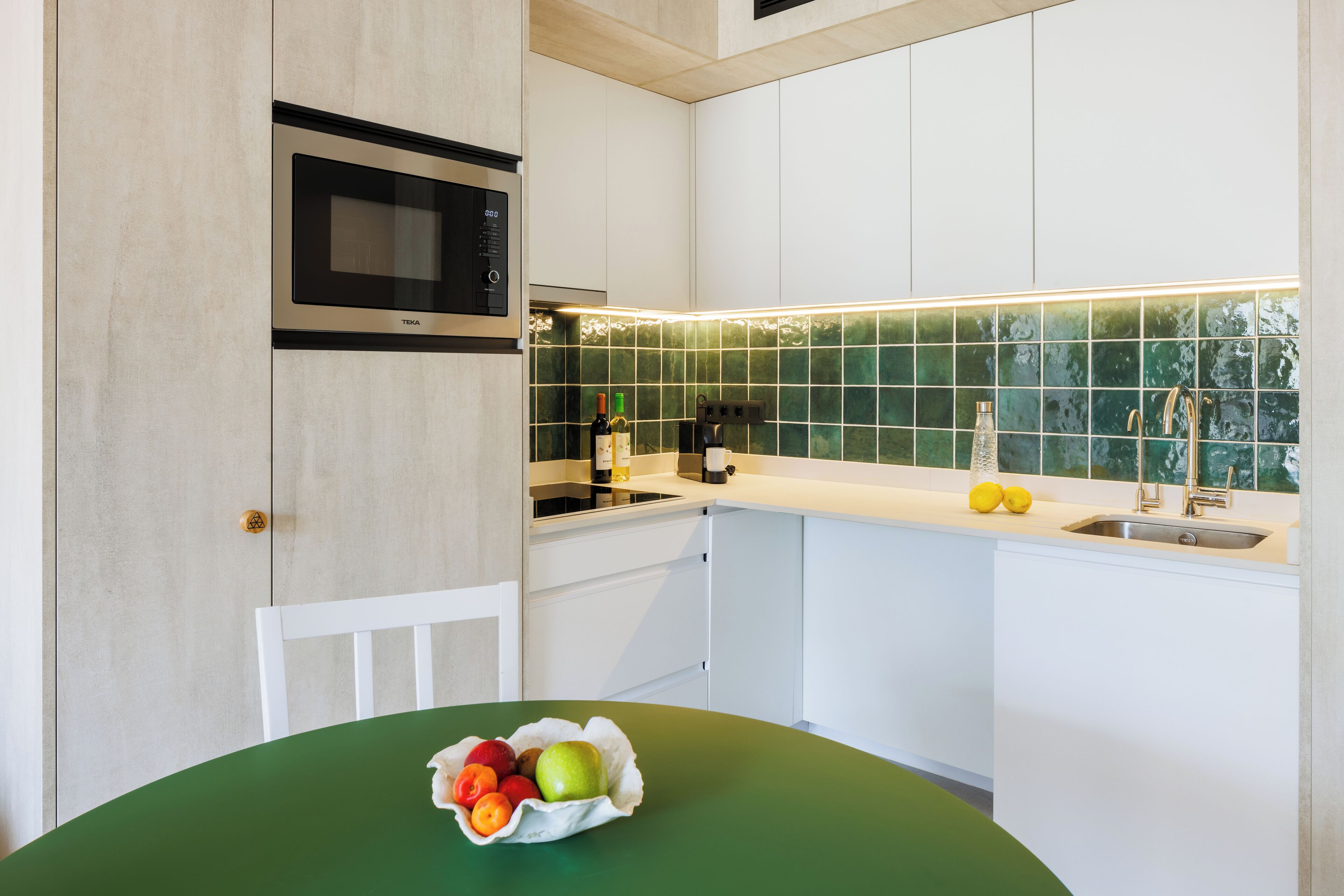 Una cocina moderna con armarios blancos, encimera verde, microondas y fregadero.