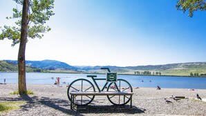 A bench with a bicycle and a sign, overlooking a lake with people in the background. - Lisi Hills Hotel (Tbilisi)
