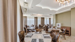 A spacious dining area with multiple tables and chairs, elegant chandeliers, and large windows with curtains. - Lisi Hills Hotel (Tbilisi)