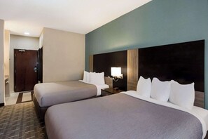 A hotel room with two beds, a nightstand, a wall-mounted lamp, and a door. - Quality Inn Galesburg Near US Highway 34 and I-74 (Galesburg)