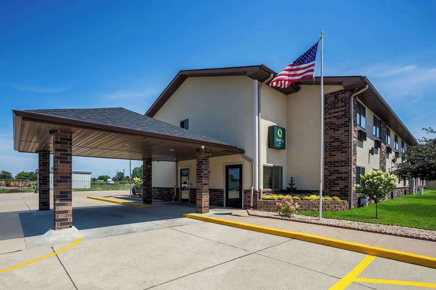 A hotel with a covered entrance, an American flag, and a sign indicating it is a Quality Inn.