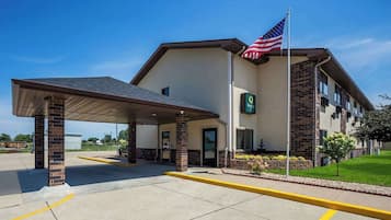 A hotel with a covered entrance, an American flag, and a sign indicating it is a Quality Inn.