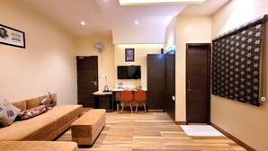 A modern living room with a sofa, a small table, and a TV. There is a door leading to a kitchen area with a fridge and a microwave. - Hotel Urban Galaxy (Amritsar)