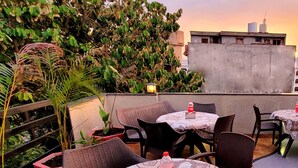 An outdoor seating area with round tables and chairs, surrounded by potted plants and a view of buildings in the background. - Hotel Urban Galaxy (Amritsar)