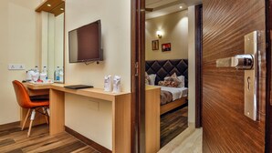 A hotel room with a wooden desk, a chair, a bed with a headboard, a television, and a door with a lock. - Hotel Urban Galaxy (Amritsar)