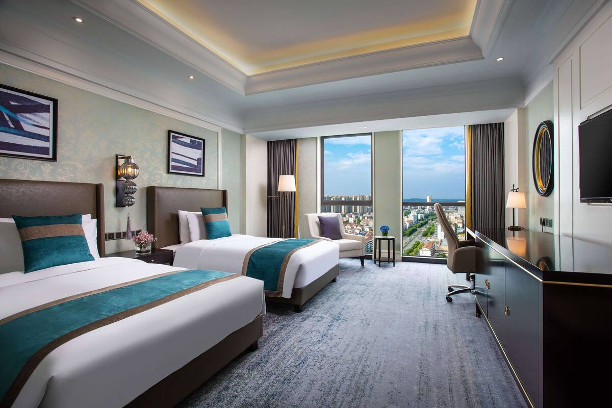 Une chambre d’hôtel avec deux lits, un bureau, une chaise, une télévision et une vue sur la ville.