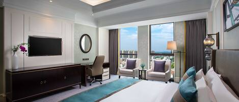 Quarto de hotel com uma cama grande, uma escrivaninha, televisão, vista da cidade e varanda.