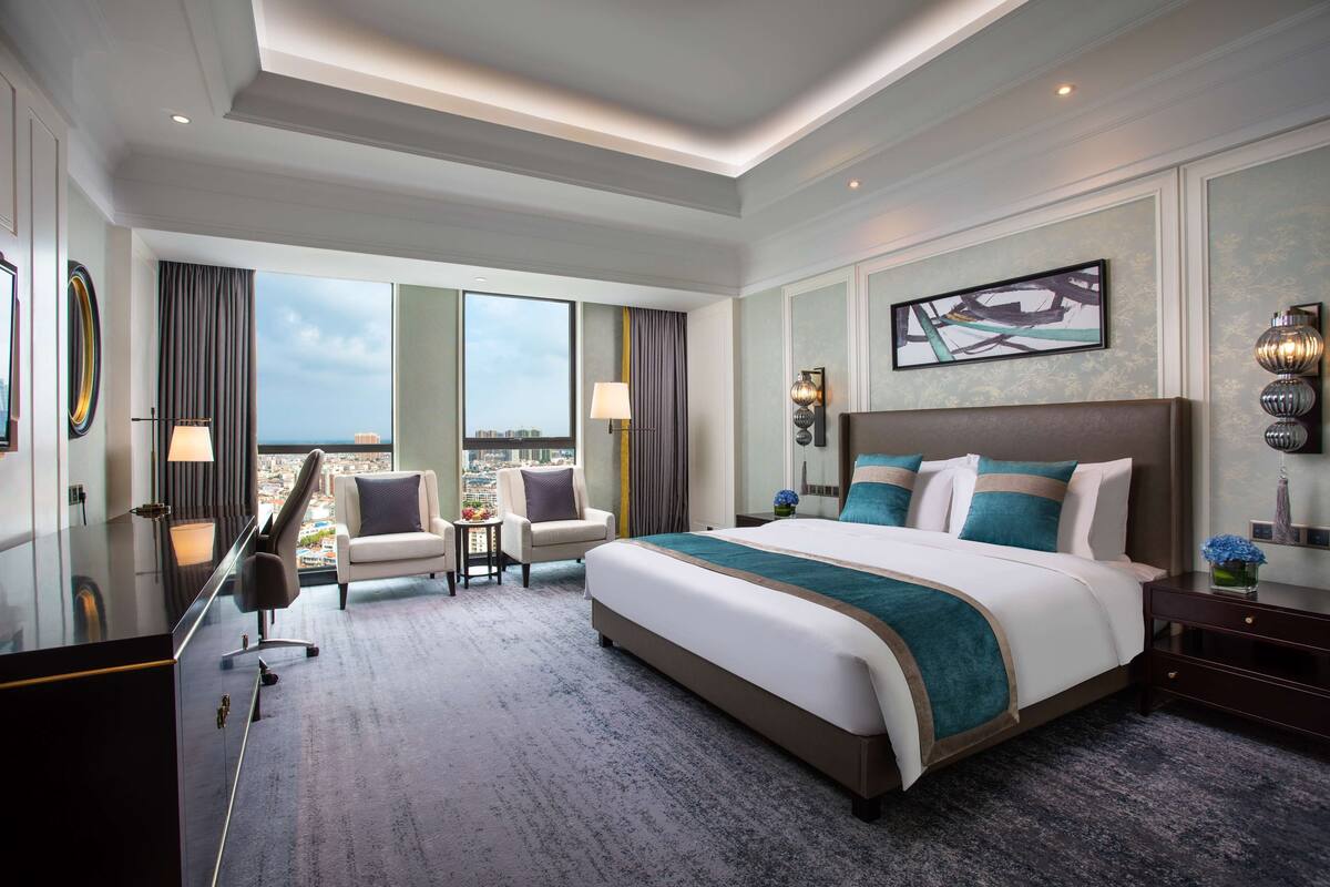 Une chambre d’hôtel spacieuse, dotée d’un grand lit, d’un bureau, d’une chaise et offrant une vue sur la ville.