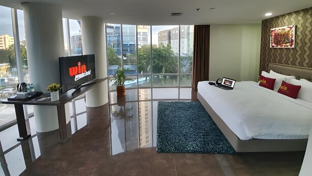 Una habitació d'hotel moderna amb un llit gran, un escriptori amb un televisor i vistes a la ciutat.