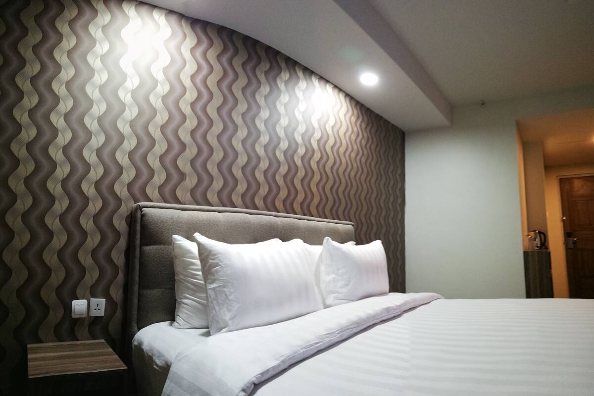 A neatly made bed with white linens in a hotel room with a curved wall featuring a wavy pattern.