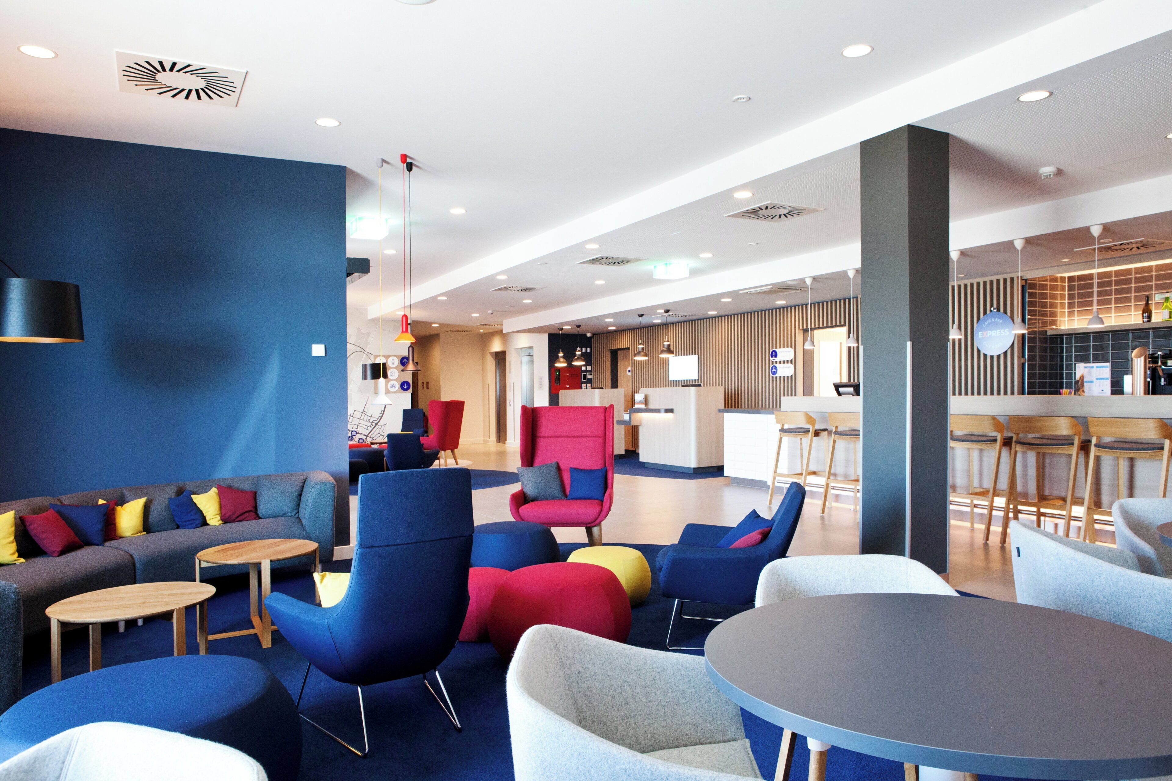 Un espacio lounge moderno con sofás, sillas y mesas, con una barra y mostrador de recepción al fondo.