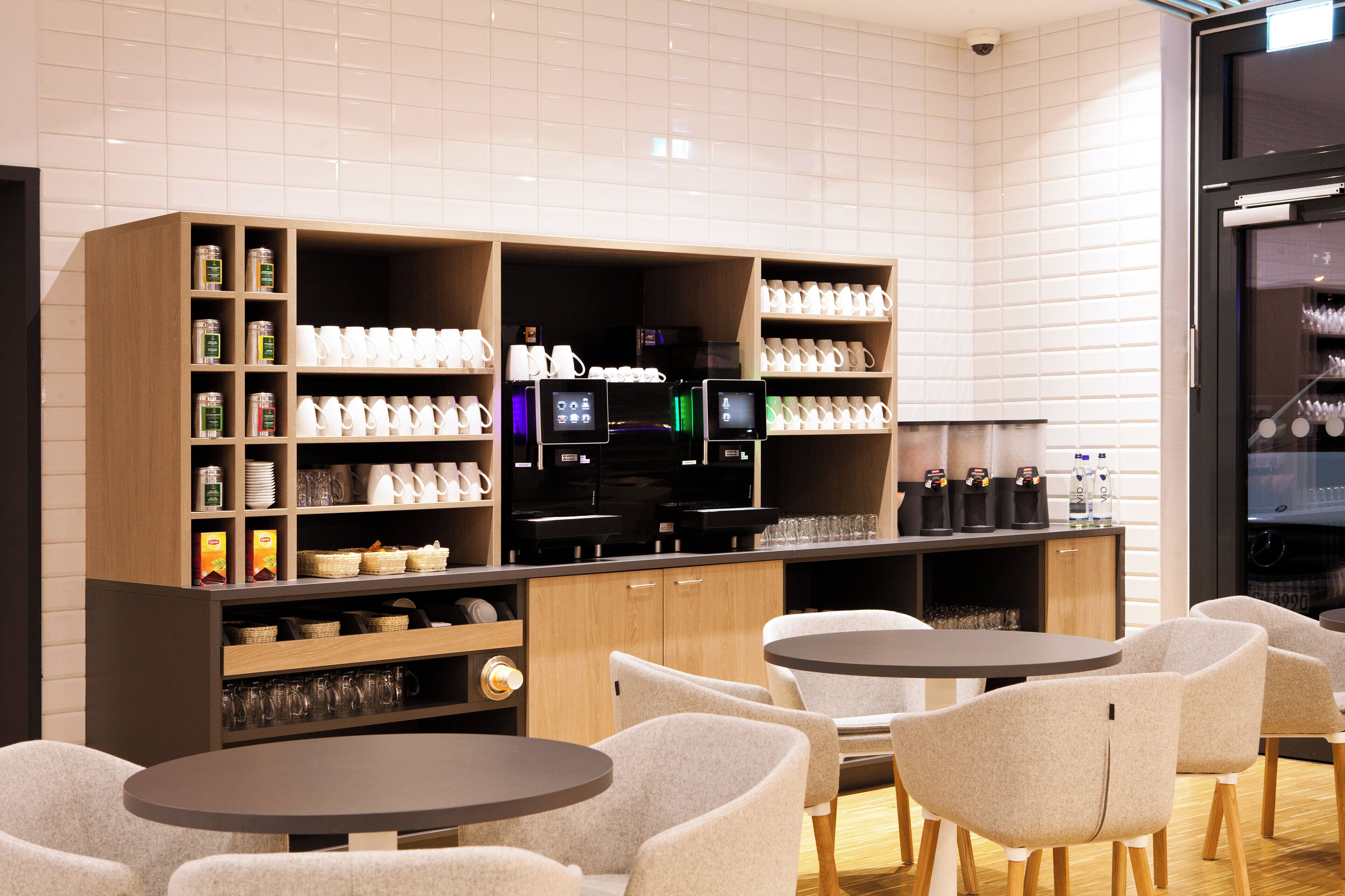 A modern cafe with round tables and chairs, a coffee machine, and shelves stocked with mugs and condiments.