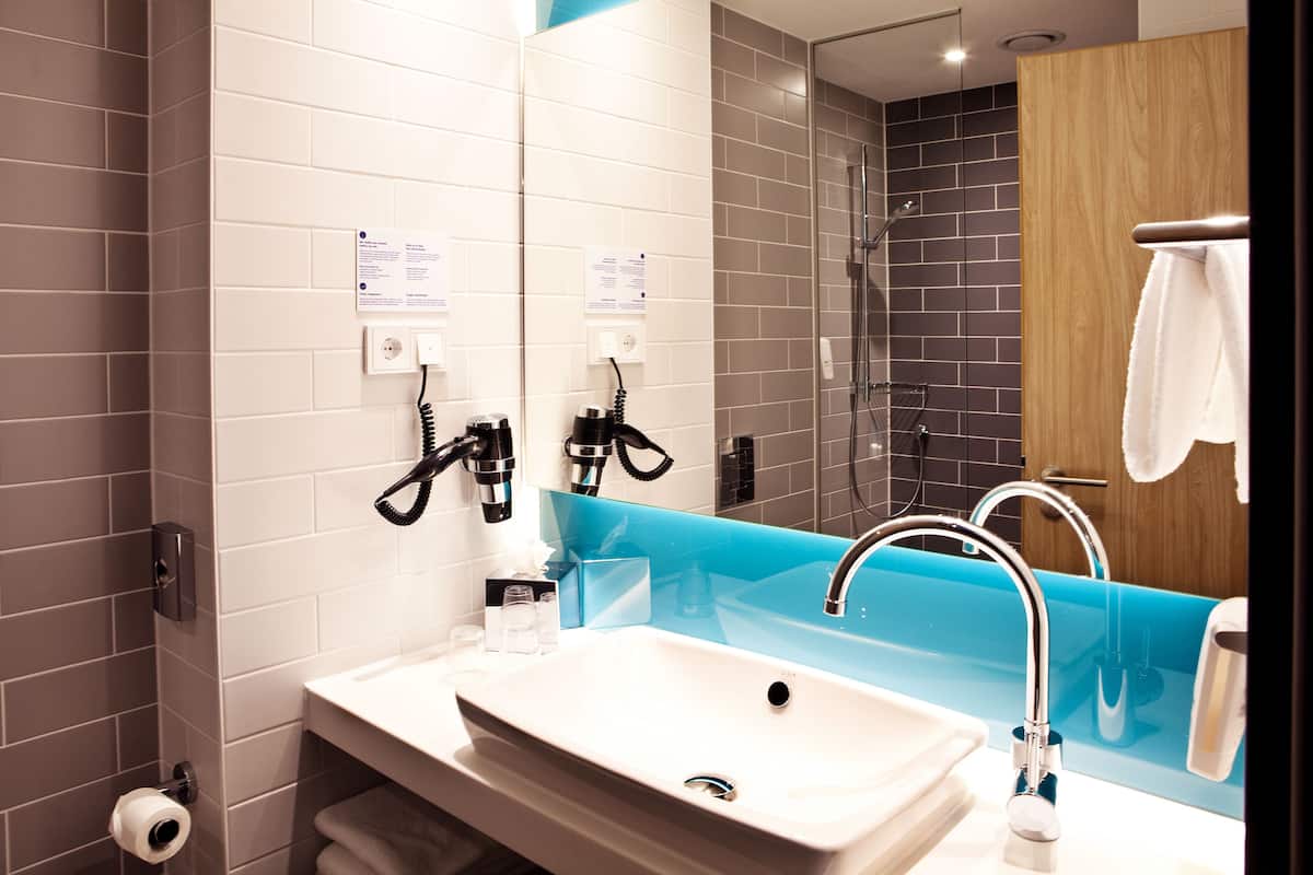 A modern bathroom with a white sink, a blue vanity, a glass shower enclosure, and a wooden door.